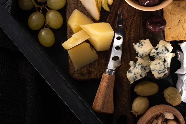 Top view of tray with knife next to pieces of cheese, slices of pear, olives, pistachios and grapes isolated on black — Stock Photo