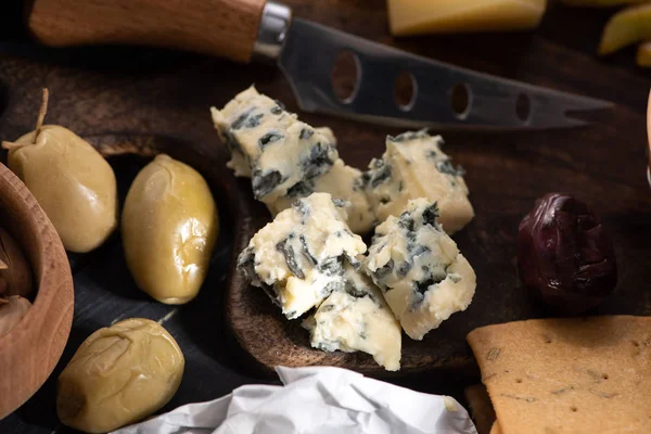 Focus selettivo di pezzi di dorblu sul tagliere con coltello, olive secche e cracker — Foto stock