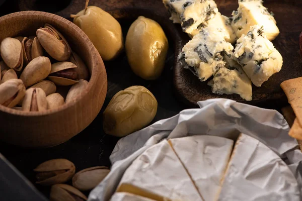 Selektiver Schwerpunkt getrockneter Oliven mit Camembert, Dorblu und Pistazien auf Holztablett — Stockfoto