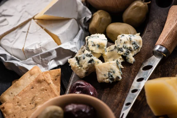 Selective focus of dorblu with knife, grana padano and olives on cutting board next to camembert and crackers — Stock Photo