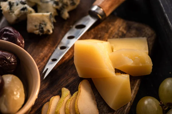 Selective focus of grana padano with knife, slices of pear, olives, grapes and dorblu on cutting board — Stock Photo