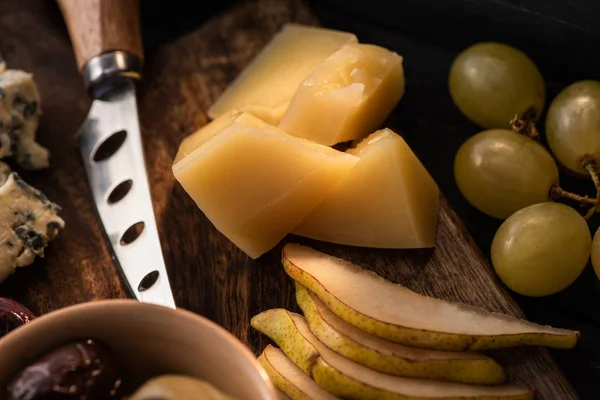 Selective focus of grana padano with pieces of pear, bowl of olives, knife, dorblu, grapes on cutting board — Stock Photo