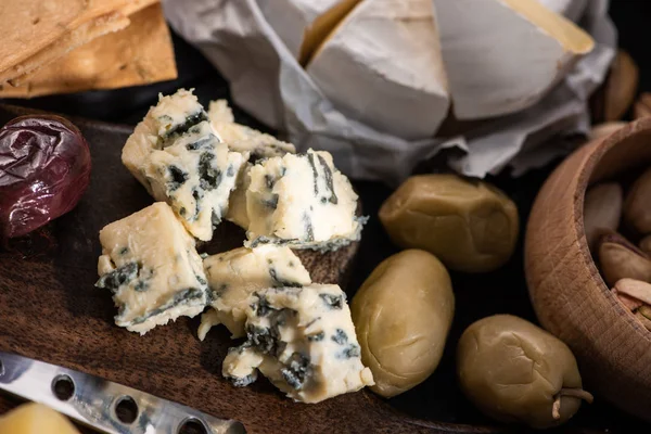 Selective focus of dorblu with dried olives, bowl of pistachios, camembert and crackers on tray — Stock Photo