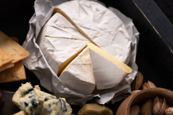 Selective focus of pieces of camembert with crackers, bowl of pistachios, dorblu and olive on tray — Stock Photo