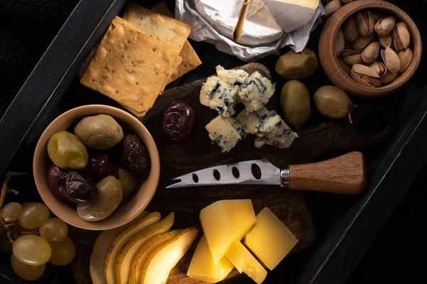 Vue de dessus de la composition alimentaire du fromage, des olives séchées, des fruits, des pistaches et des craquelins sur plateau en bois — Photo de stock