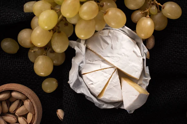 Top view of pieces of camembert with grapes and bowl of pistachios isolated on black — Stock Photo