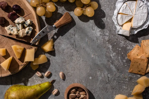 Vista superior de queso, frutas, nueces, galletas y aceitunas con cuchillo y tabla de cortar sobre fondo gris - foto de stock