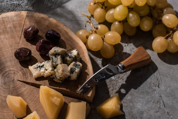 Grana Padano und Dorblu mit Oliven und Messer auf rundem Holzbrett neben Trauben auf grauem Hintergrund — Stockfoto