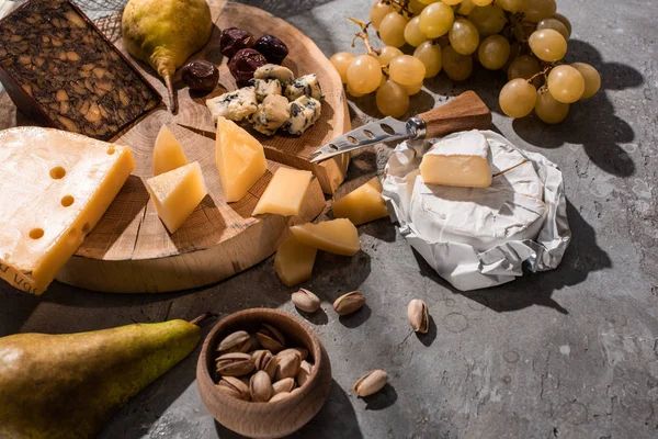Diferentes tipos de queso con frutas, aceitunas, pistachos, sobre tabla de madera sobre fondo gris - foto de stock