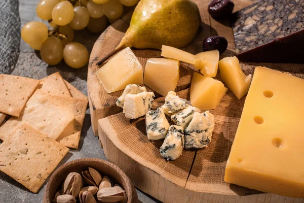Selective focus of different kinds of cheese with pear and olives on wooden board next to grapes, nuts and crackers — Stock Photo