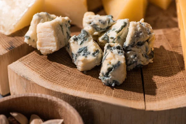 Selective focus of pieces of dorblu with grana padano on wooden board next to bowl of pistachios — Stock Photo