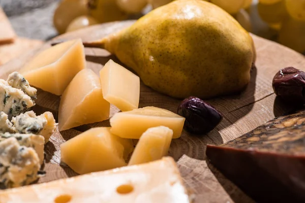 Selektiver Schwerpunkt verschiedener Käsesorten mit getrockneten Oliven und Birnen auf rundem Holzbrett — Stockfoto