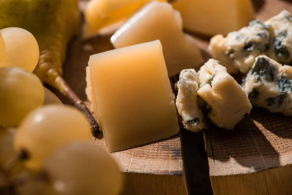 Selective focus of grapes, pear, pieces of grana padano and dorblu on wooden background — Stock Photo