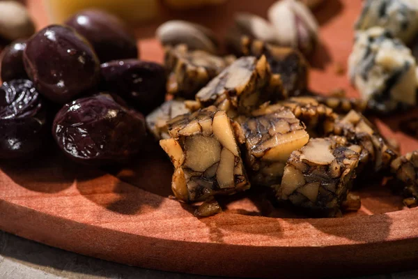 Selective focus of pieces of nut cheese with olives on round wooden board — Stock Photo