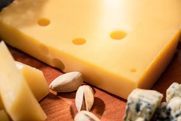 Selective focus of different kinds of cheese with pistachios on wooden background — Stock Photo