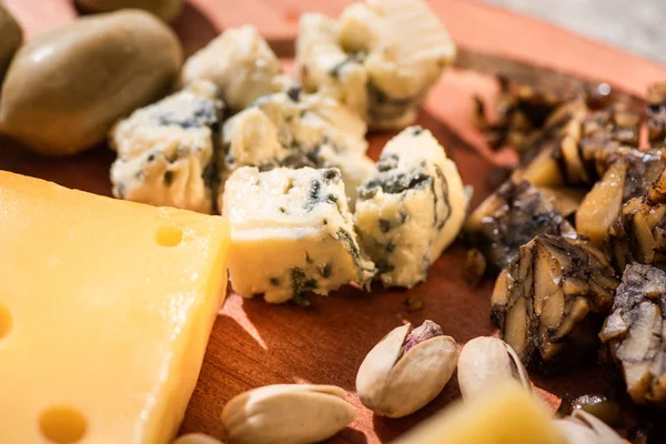 Enfoque selectivo de trozos de queso, pistachos y aceitunas sobre fondo de madera - foto de stock