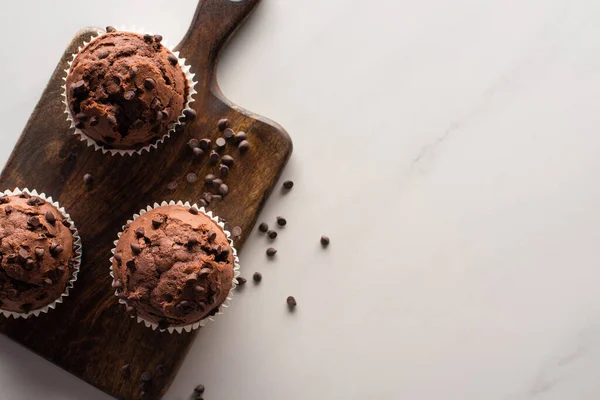 Vista superior de muffins de chocolate fresco en tabla de cortar de madera en la superficie de mármol - foto de stock