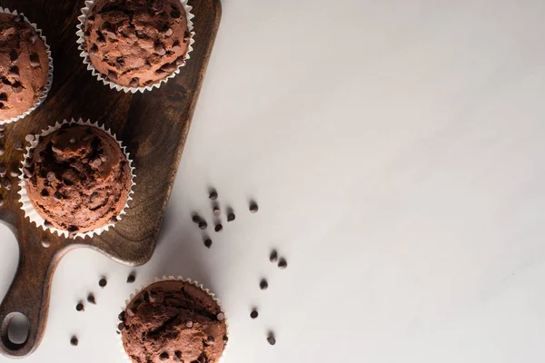 Vista superior de muffins de chocolate fresco na placa de corte de madeira na superfície de mármore — Fotografia de Stock