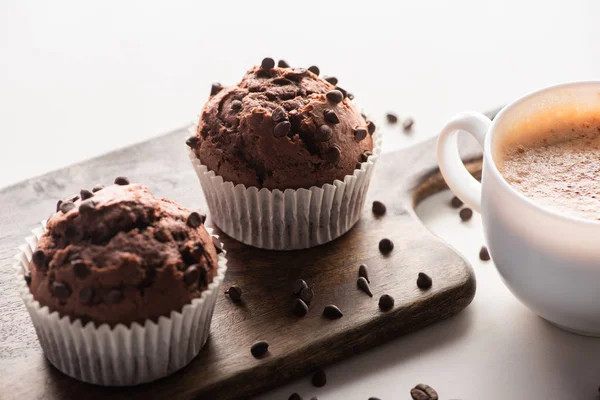 Fresh chocolate muffins on wooden cutting board near cappuccino — Stock Photo