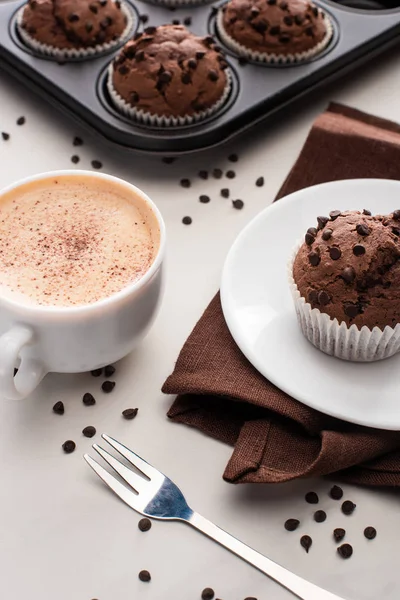 Свежие шоколадные кексы в олове из кексов, коричневая салфетка с тарелкой рядом с кофе и вилкой — стоковое фото