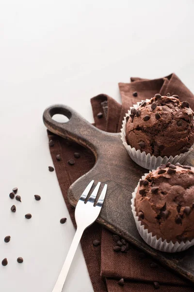 Fresh chocolate muffins on wooden cutting board on brown napkin with fork — Stock Photo