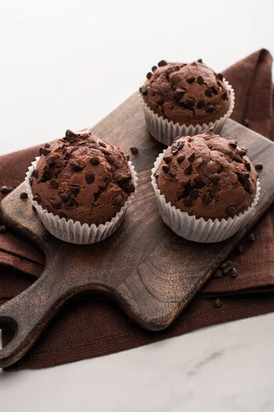 Fresh chocolate muffins on wooden cutting board on brown napkin — Stock Photo