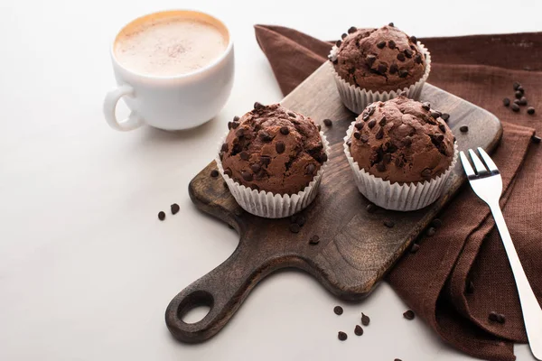 Fresh chocolate muffins on wooden cutting board near napkin, fork and coffee — Stock Photo