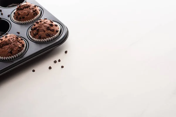 Magdalenas de chocolate fresco en lata de magdalenas en la superficie blanca - foto de stock