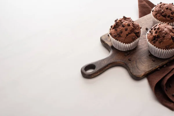 Fresh chocolate muffins on wooden cutting board near brown napkin — Stock Photo