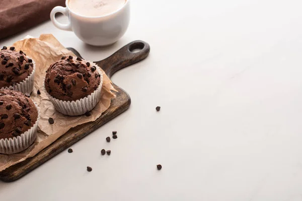 Fresh chocolate muffins on wooden cutting board near coffee — Stock Photo