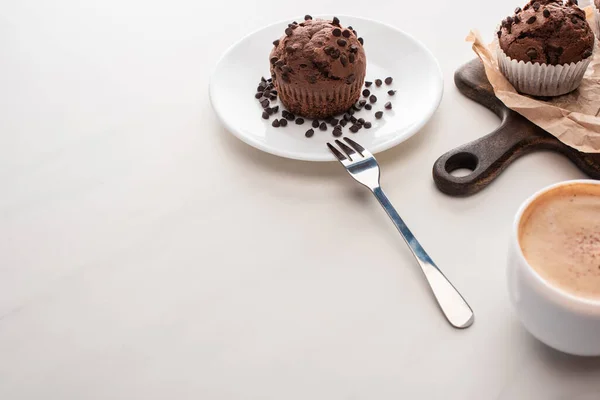 Muffins de chocolate fresco na placa de corte de madeira e placa com garfo perto de café — Fotografia de Stock