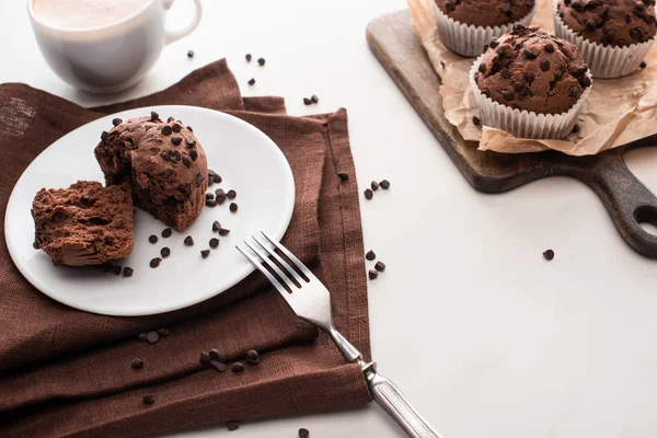 Frische Schokoladenmuffins auf hölzernem Schneidebrett neben Teller mit Gabel und Kaffee — Stockfoto