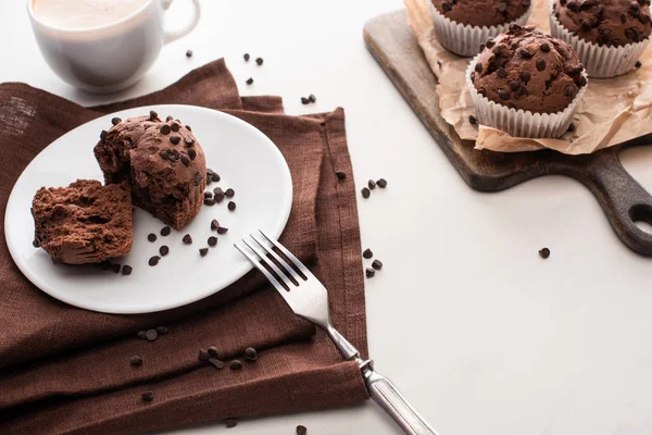 Fresh chocolate muffins on wooden cutting board near plate with fork and coffee — Stock Photo