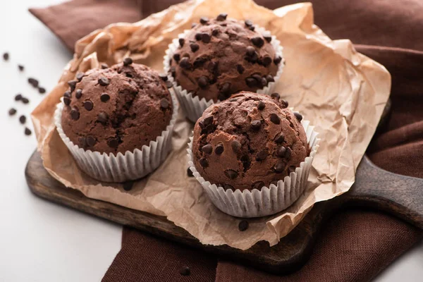 Fresh chocolate muffins on wooden cutting board on brown napkin — Stock Photo