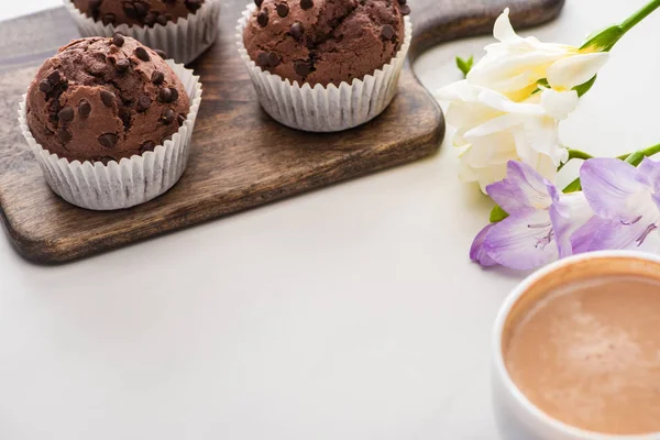 Frische Schokoladenmuffins auf Holzschneidebrett in der Nähe von Blumen und Kaffee — Stockfoto