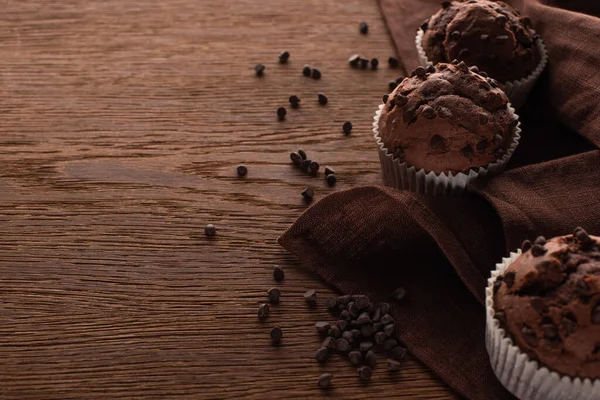 Fresh chocolate muffins on wooden surface with brown napkin — Stock Photo