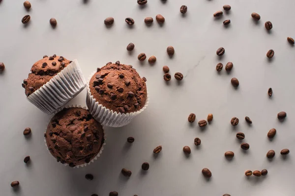 Vue de dessus des muffins au chocolat frais avec grains de café sur la surface du marbre — Photo de stock