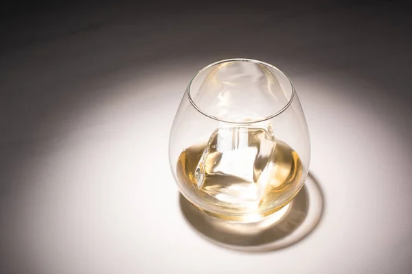 Transparent glass with ice cube and whiskey on white table with shadow — Stock Photo