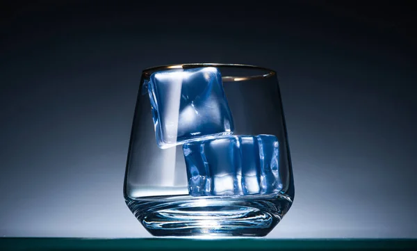 Vidrio transparente con cubitos de hielo en oscuro con luz de fondo azul - foto de stock