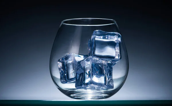 Transparent glass with ice cubes in dark with blue back light — Stock Photo