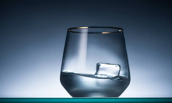 Transparent glass with ice cube and vodka in dark with back light — Stock Photo