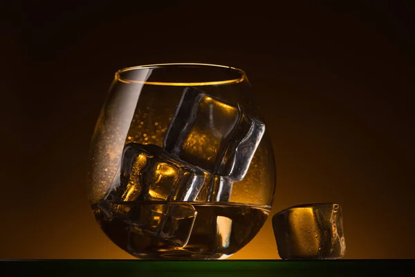 Transparent glass with ice cubes and vodka in dark with warm back light — Stock Photo