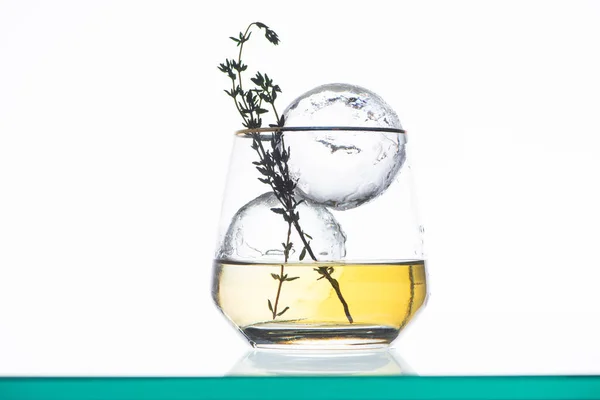 Transparent glass with golden liquid, herb and round ice isolated on white — Stock Photo