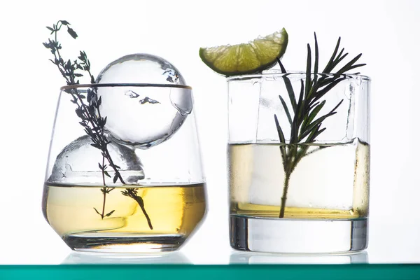 Verres transparents avec liquide doré, herbes et glace isolés sur blanc — Photo de stock