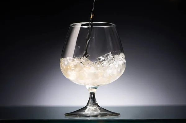 Uísque derramando em vidro transparente com gelo no escuro com luz traseira — Fotografia de Stock