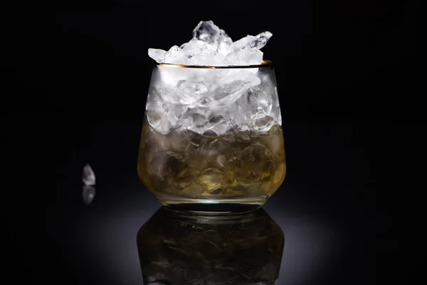 Verre transparent avec glace et liquide doré sur fond noir — Photo de stock