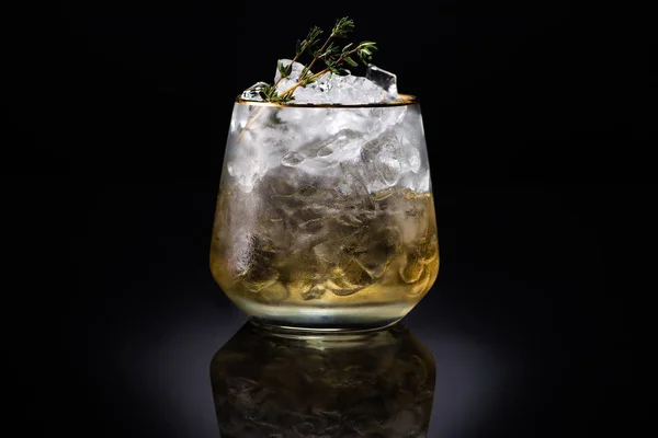 Transparent glass with ice and golden liquid garnished with herb on black background — Stock Photo