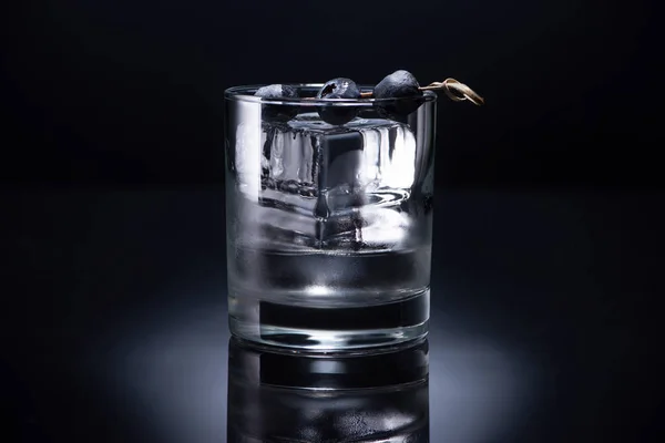 Verre transparent avec glaçon et vodka garnie de bleuets sur fond noir — Photo de stock