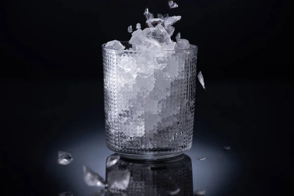Faceted glass with smashed ice on black background — Stock Photo