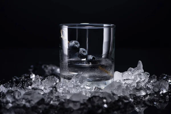 Verre transparent avec vodka et bleuets près de glace fracassée isolé sur noir — Photo de stock